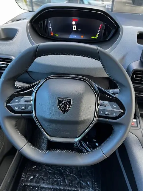 Vue rapprochée du volant cuir noir du Peugeot Rifter 2024 avec tableau de bord numérique et commandes intégrées.