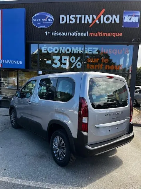 Vue 3/4 arrière droite d’un Peugeot Rifter gris foncé 2024 stationné devant une vitrine avec enseigne Distinxion.
