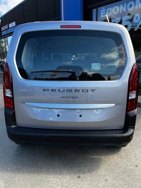 Vue arrière d'un Peugeot Rifter gris foncé 2024 avec hayon vitré et feux arrière verticaux rouges.
