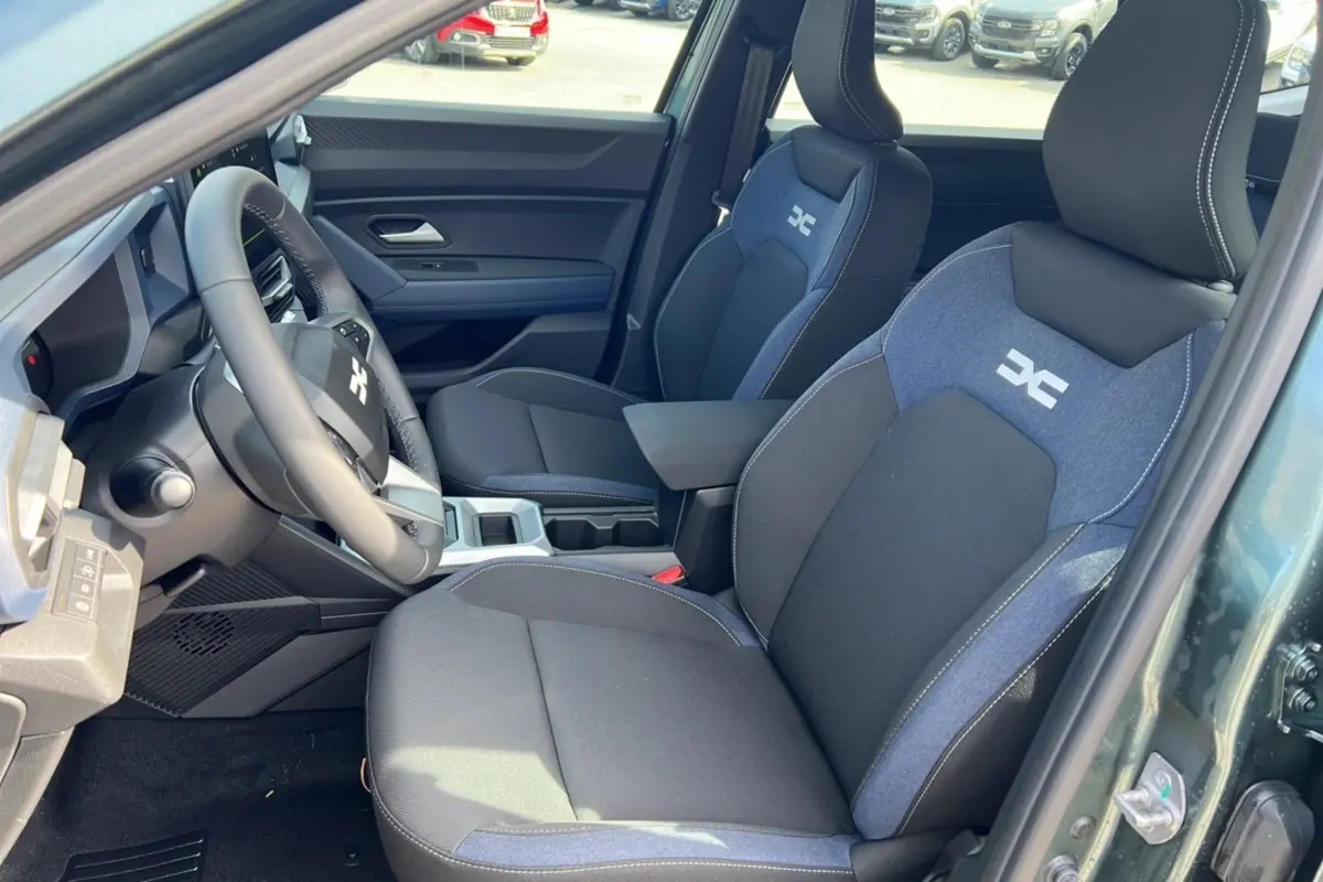 Vue intérieure côté conducteur du Dacia Bigster Hybrid 155 Expression Plus avec sièges tissu noir et bleu et accoudoir central.