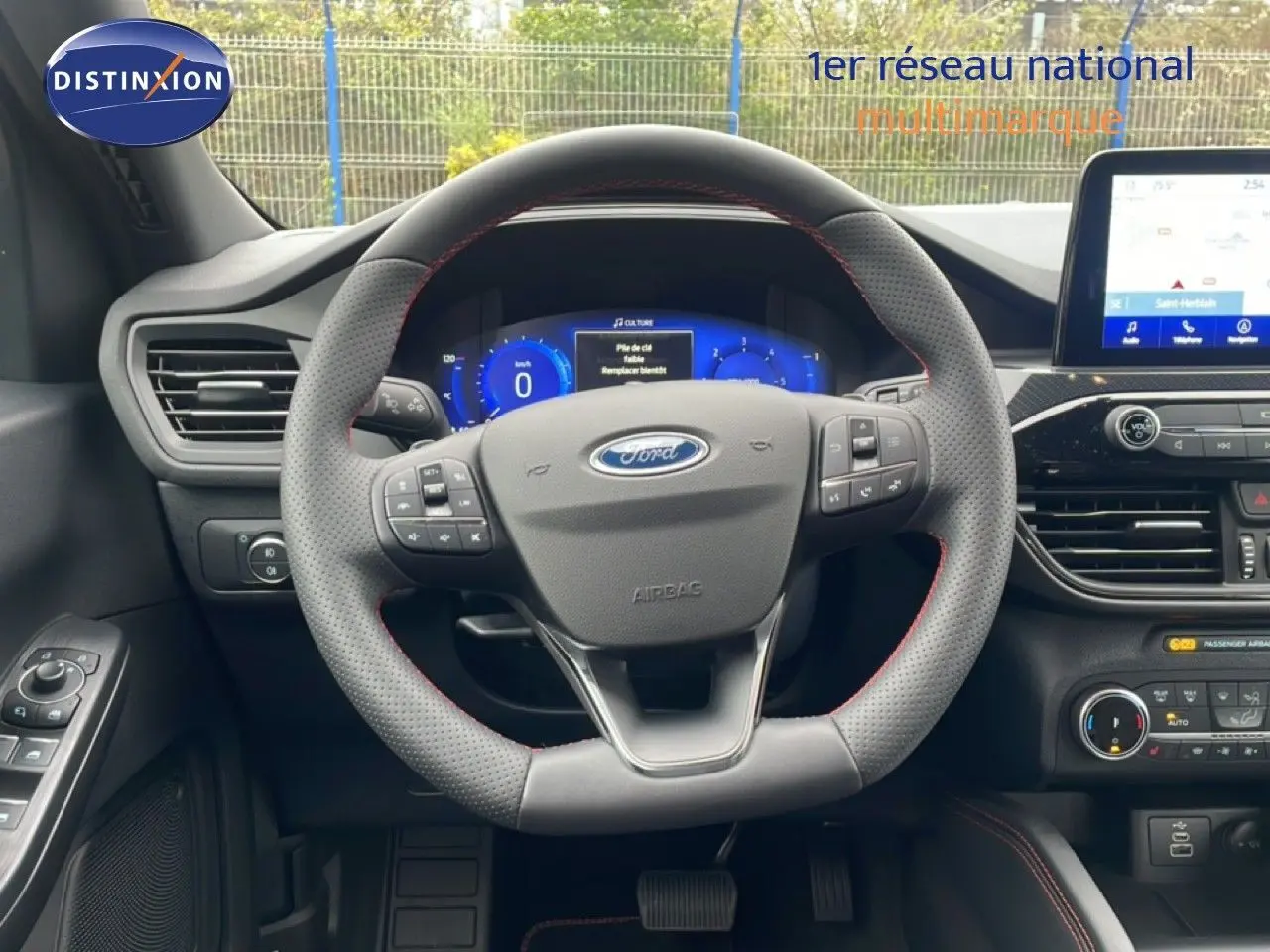Vue intérieure centrée sur le volant perforé avec coutures rouges du Ford Kuga 2024, tableau de bord digital et écran tactile visibles.
