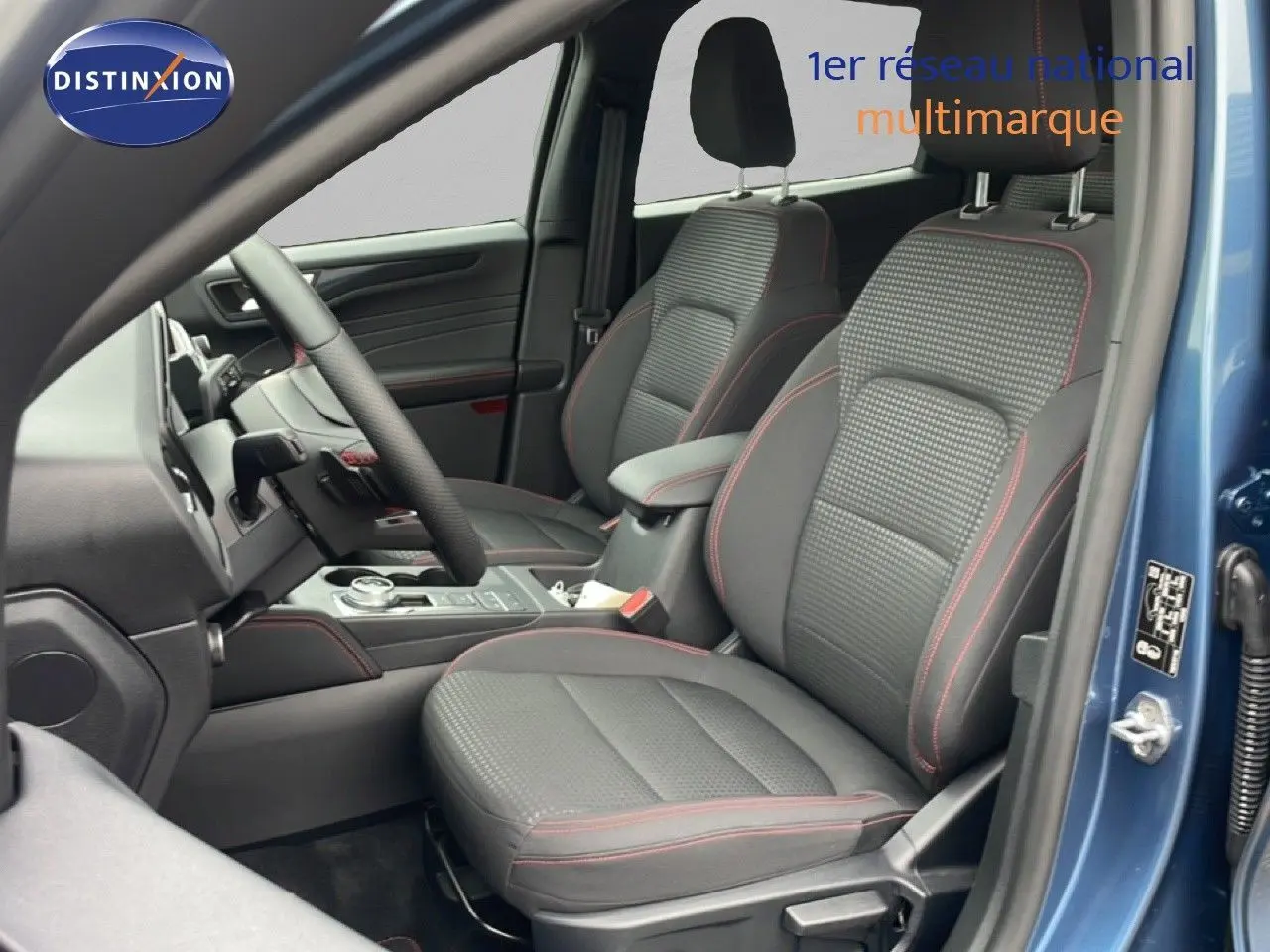 Vue intérieure côté conducteur du Ford Kuga 2024 bleu Vapor Metal, sièges tissu noir avec surpiqûres rouges et console centrale visible.