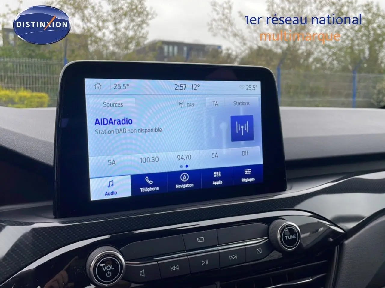 Écran tactile central du tableau de bord du Ford Kuga 2024 avec interface multimédia affichée en extérieur flou.