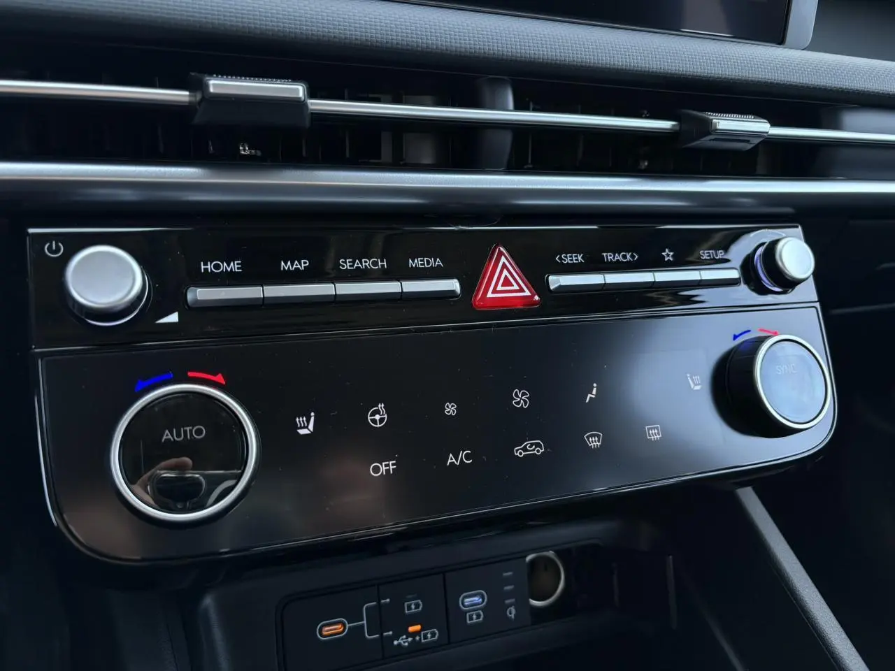 Gros plan sur la console centrale noire brillante du Hyundai Tucson 2025 avec commandes climatisation et multimédia.