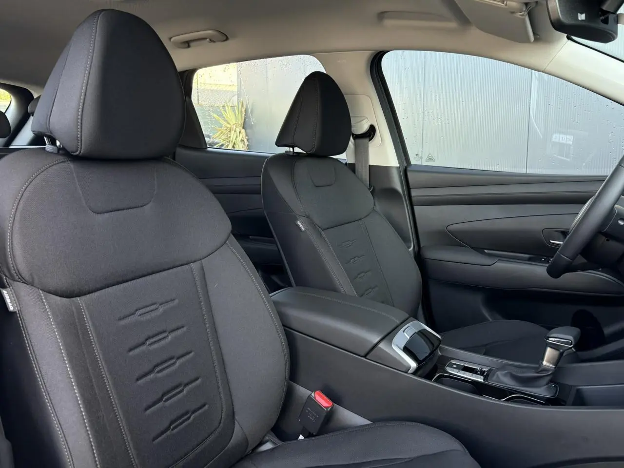 Intérieur du Hyundai Tucson 2025 vu côté passager, sièges noirs en tissu avec console centrale et levier de vitesses.