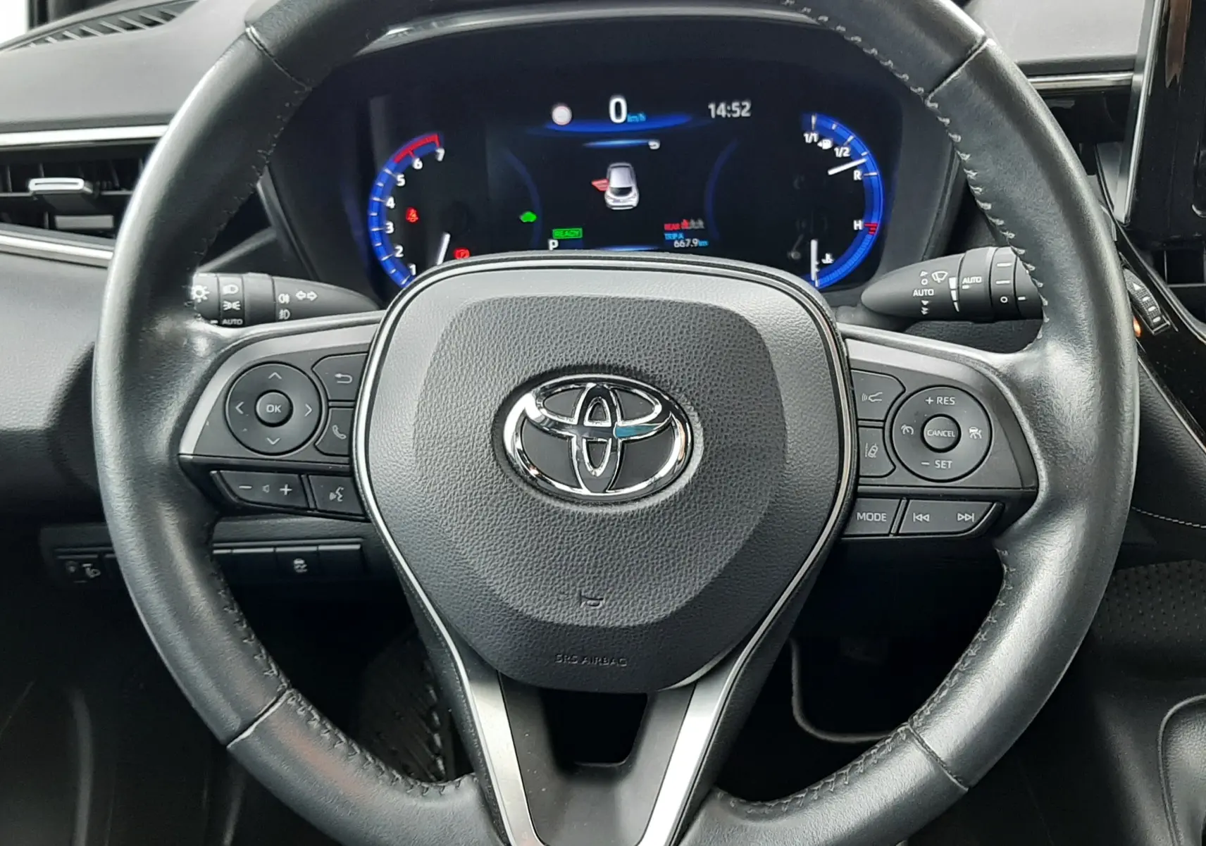 Vue rapprochée du volant en cuir noir d'une Toyota Corolla 122 CH Dynamic 2022 avec tableau de bord digital éclairé.