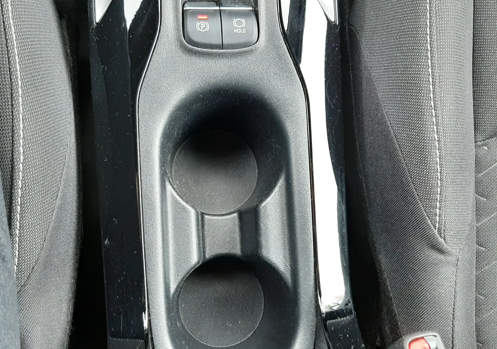 Gros plan sur la console centrale noire de la Toyota Corolla blanche 2022, avec porte-gobelets et boutons de frein à main électronique.