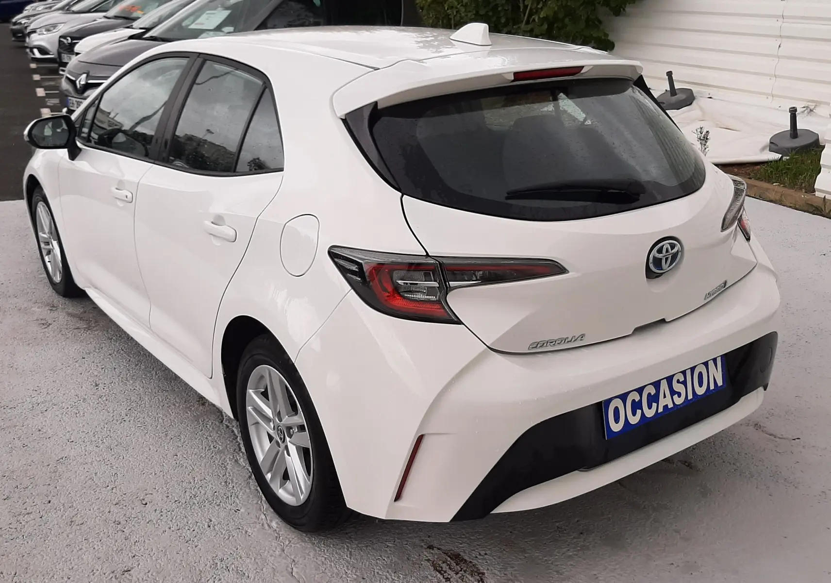 Vue 3/4 arrière droite d'une Toyota Corolla blanche hybride 2022 avec hayon et feux arrière LED, en stationnement.