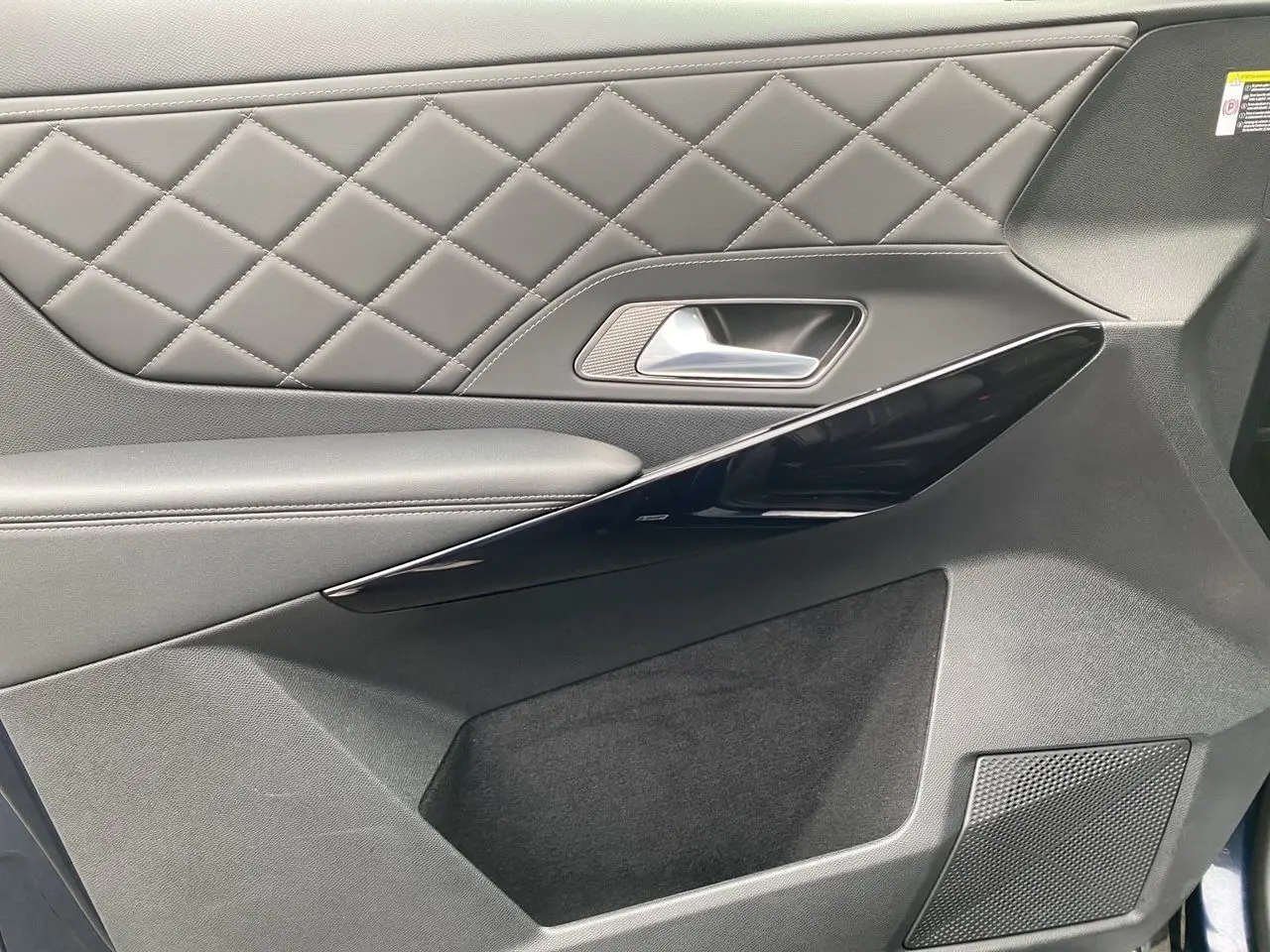 Gros plan sur la garniture de porte côté droit du DS7 2024 en cuir noir matelassé avec insert laqué noir.