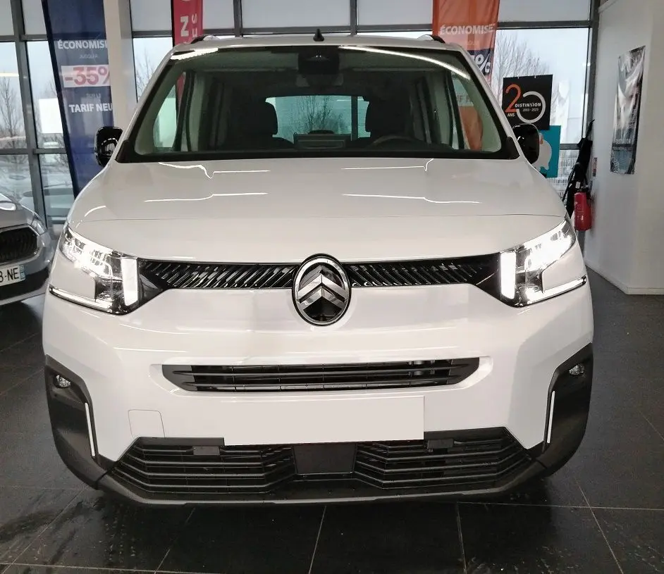 Vue avant d'un Citroën Berlingo blanc 2025 avec calandre noire et phares LED allumés en intérieur showroom.