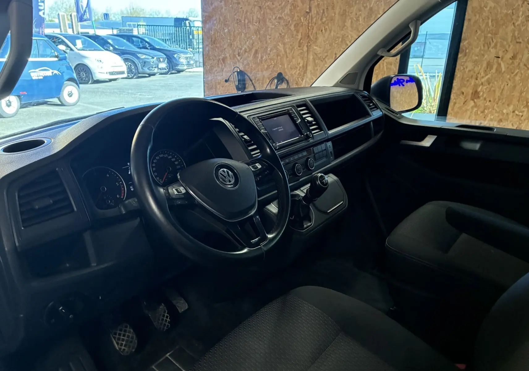 Vue intérieure côté conducteur du Volkswagen Multivan T6 PH.1 noir, montrant le volant, tableau de bord et levier de vitesses manuel.