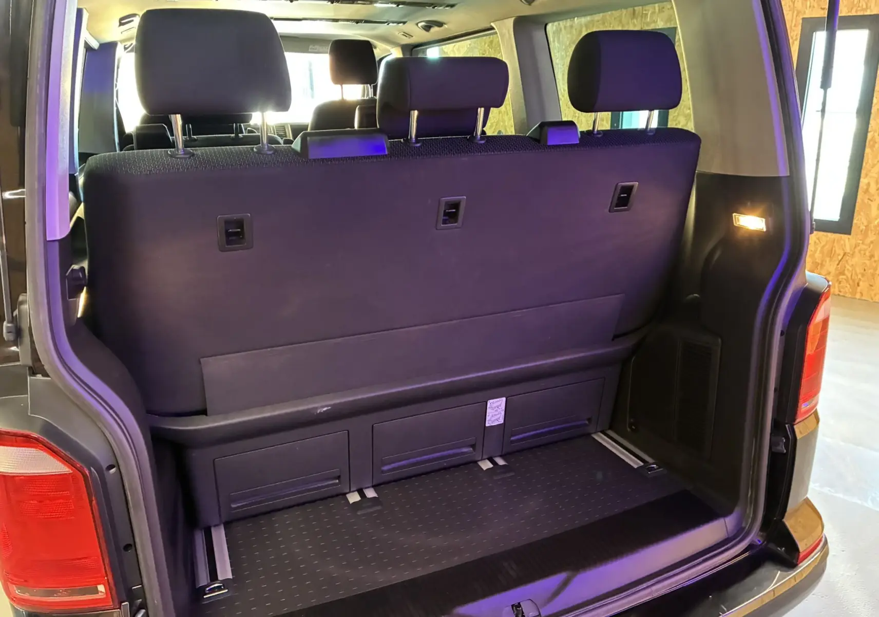 Vue arrière ouverte du Volkswagen Multivan T6 noir montrant la banquette arrière et le coffre intérieur spacieux.