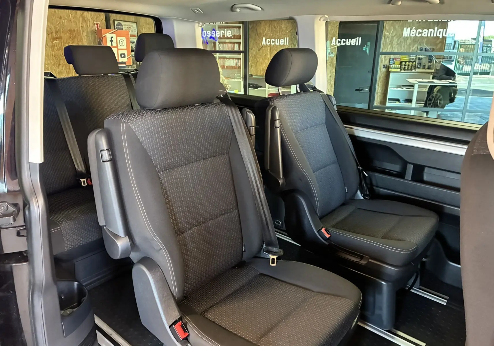 Vue intérieure du Volkswagen Multivan T6 PH.1 noir, montrant les sièges passagers avant et arrière en tissu noir.