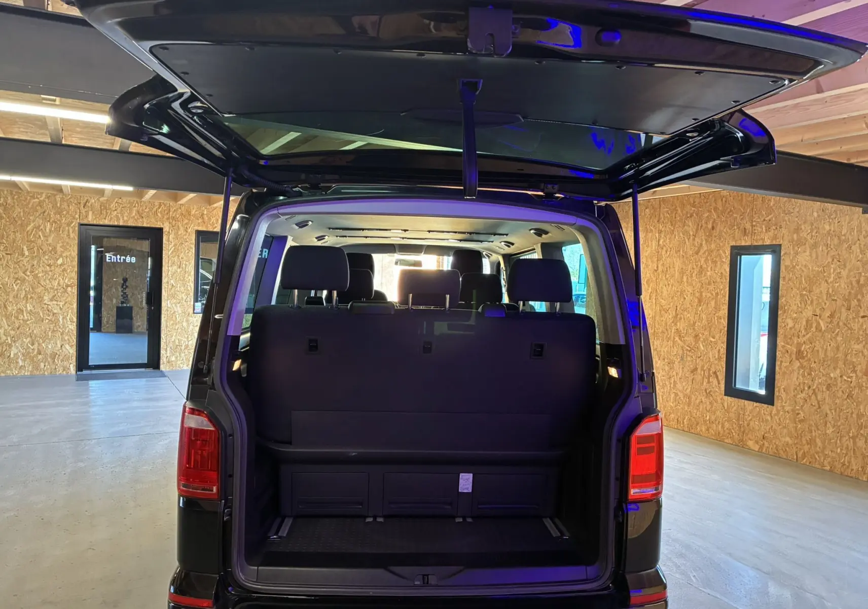 Vue arrière du Volkswagen Multivan T6 PH.1 noir de 2015 avec hayon ouvert, montrant l'espace intérieur et les sièges.