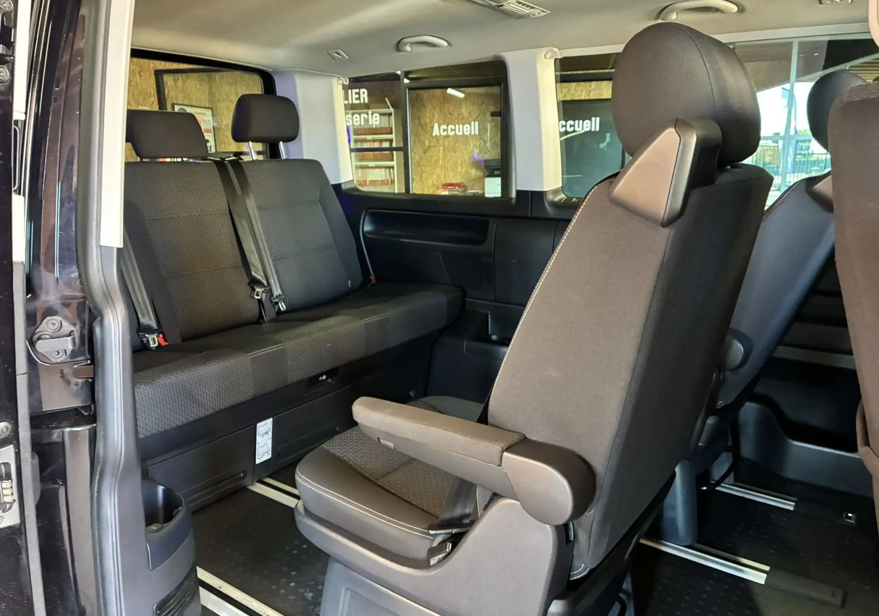 Vue intérieure côté gauche du Volkswagen Multivan T6 noir, montrant les sièges arrière et une banquette trois places.