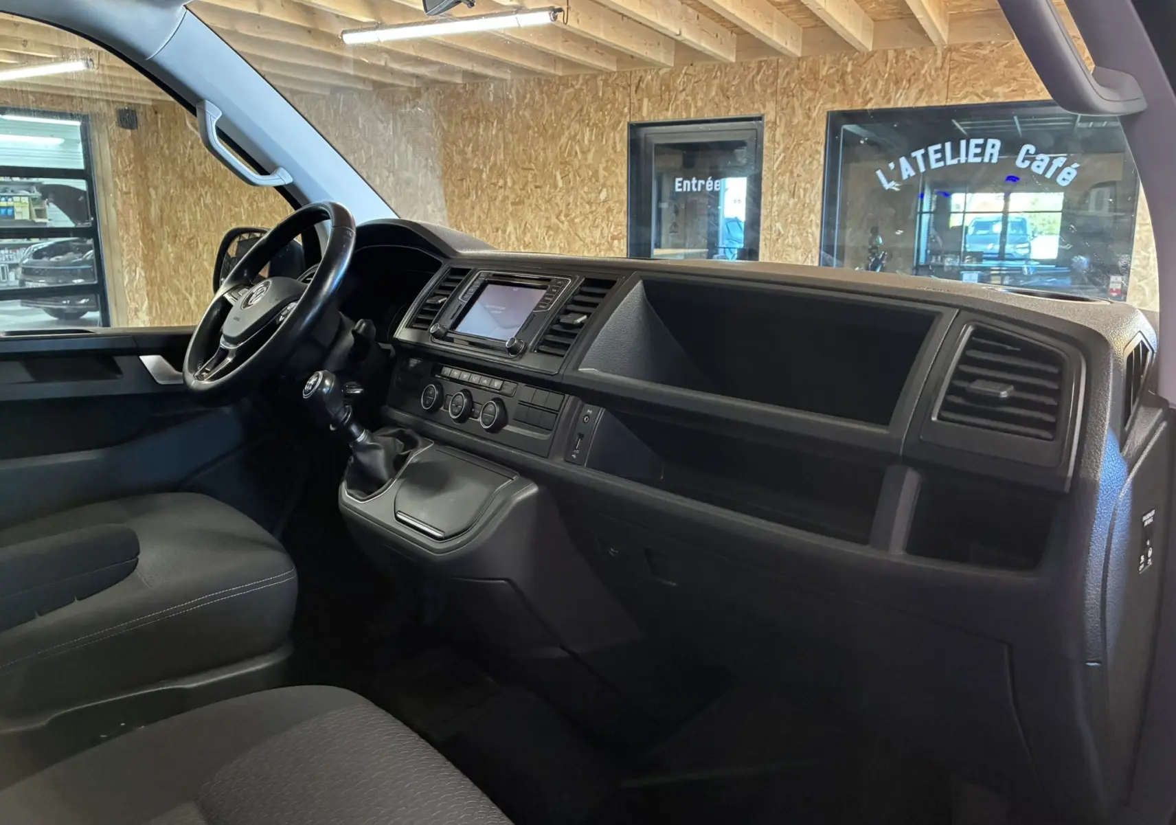 Vue intérieure côté conducteur du Volkswagen Multivan T6 PH.1 noir, montrant le tableau de bord et la boîte manuelle.