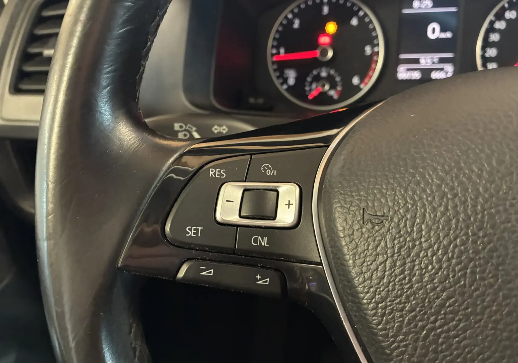 Gros plan sur les commandes de régulateur de vitesse au volant noir du Volkswagen Multivan T6 PH.1 2015, tableau de bord en arrière-plan.