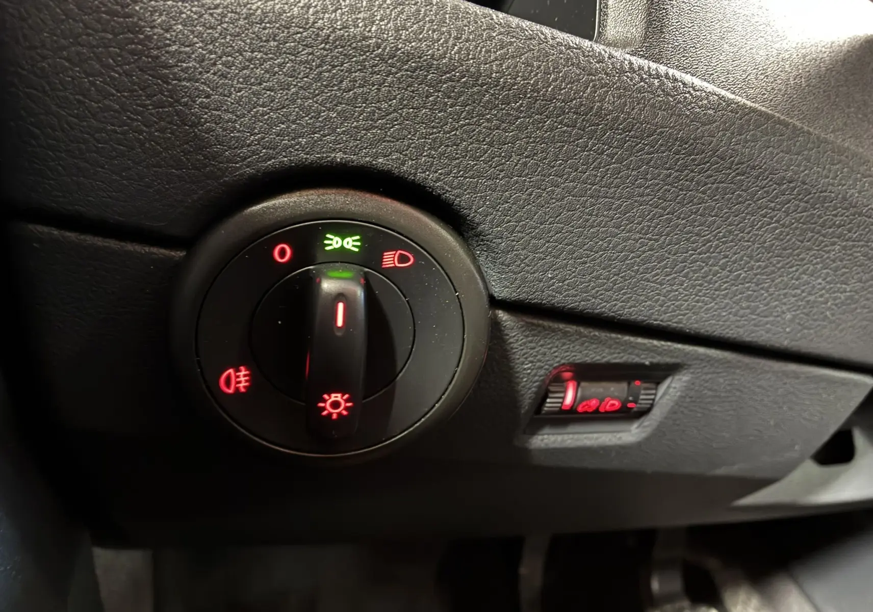 Gros plan sur le sélecteur d'éclairage noir du tableau de bord du Volkswagen Multivan T6 PH.1, avec voyants lumineux rouges et verts.