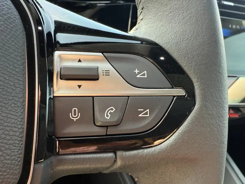 Gros plan sur les commandes du volant à droite de la Peugeot 308 hybride 2025, avec boutons de volume et appels en noir et gris.