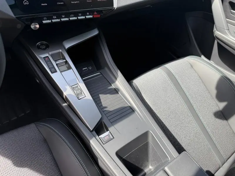 Vue intérieure centrée sur la console centrale et siège avant droit de la Peugeot 308 Hybrid 2025 en tissu gris et surpiqûres vertes.