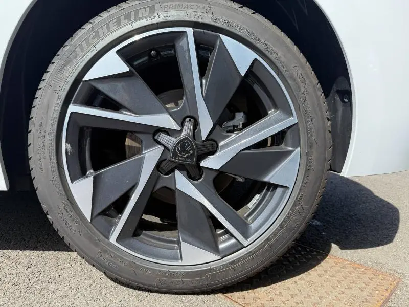 Gros plan sur la roue avant droite d'une Peugeot 308 1.2 Hybrid 145ch Allure blanche, jante alliage bicolore au design moderne.