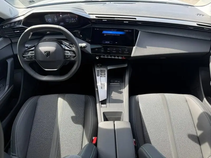 Vue intérieure avant de la Peugeot 308 Hybrid 2025, tableau de bord moderne avec écran tactile et volant compact noir.