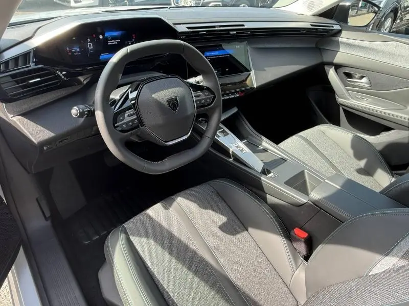 Vue intérieure côté conducteur du Peugeot 308 1.2 Hybrid 145ch Allure 2025, avec volant compact et tableau de bord numérique.