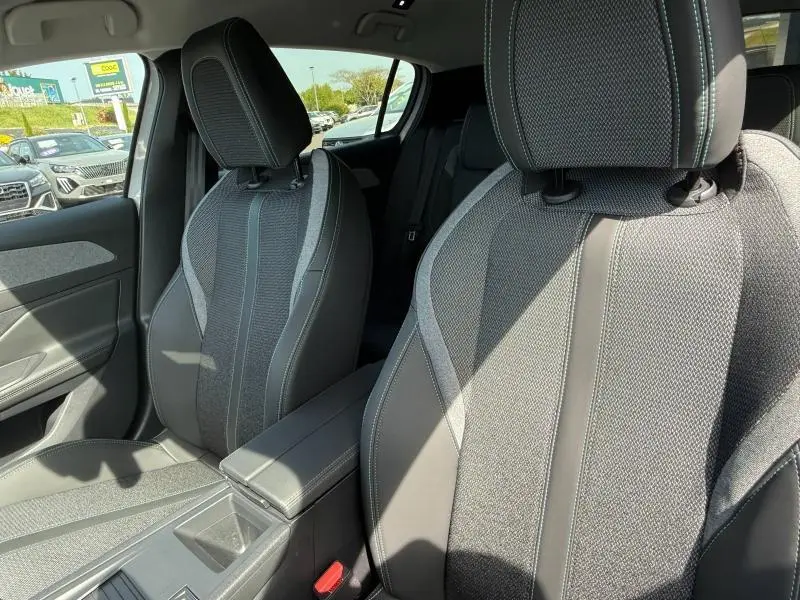 Vue intérieure rapprochée des sièges avant en tissu gris avec surpiqûres, dans une Peugeot 308 blanche 2025 hybride.