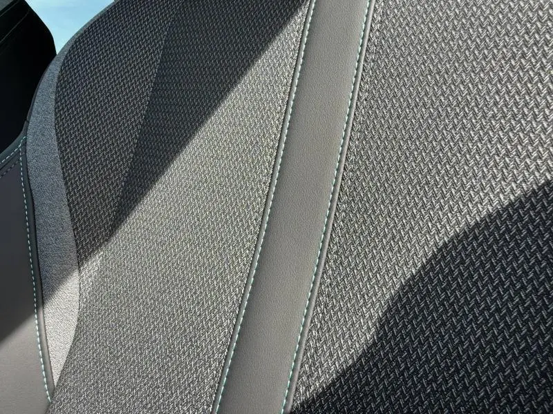 Gros plan sur le tissu gris texturé et les surpiqûres vertes du siège avant d'une Peugeot 308 Hybrid 2025.