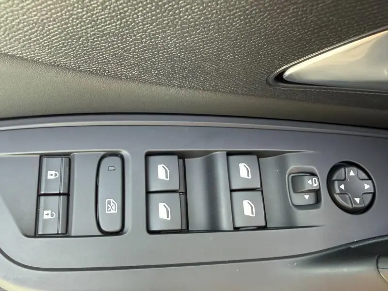 Gros plan sur les commandes de lève-vitres et rétroviseurs côté conducteur d’une Peugeot 308 blanche, tableau de bord noir.