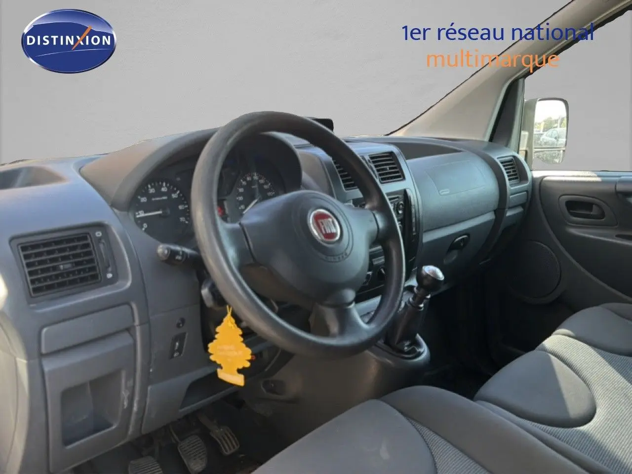 Vue intérieure côté conducteur du Fiat Scudo Fourgon gris métal, montrant le volant, tableau de bord et sièges tissu.