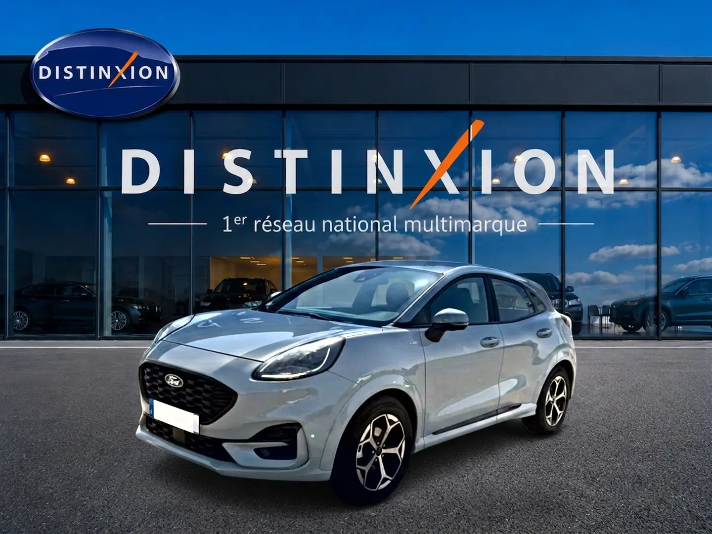 Ford Puma gris cactus en 3/4 avant droit, avec jantes alu et calandre noire, devant une vitrine Distinxion.