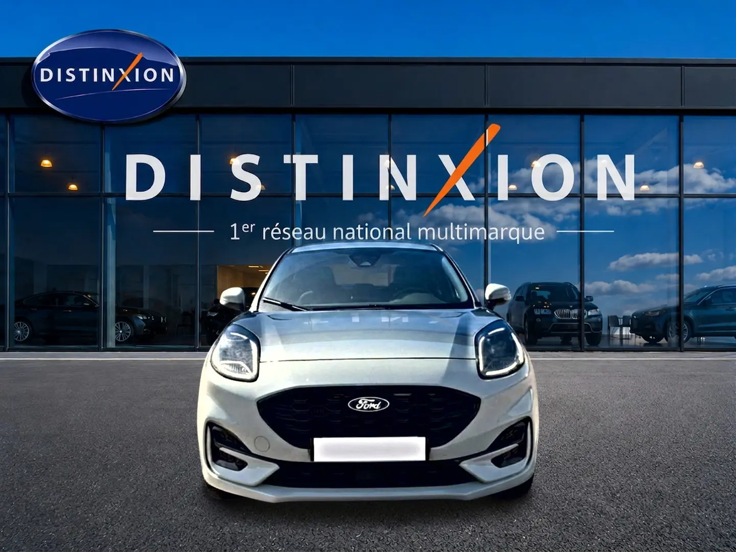 Vue frontale d'un Ford Puma gris cactus avec calandre noire et phares LED, devant une vitrine Distinxion.