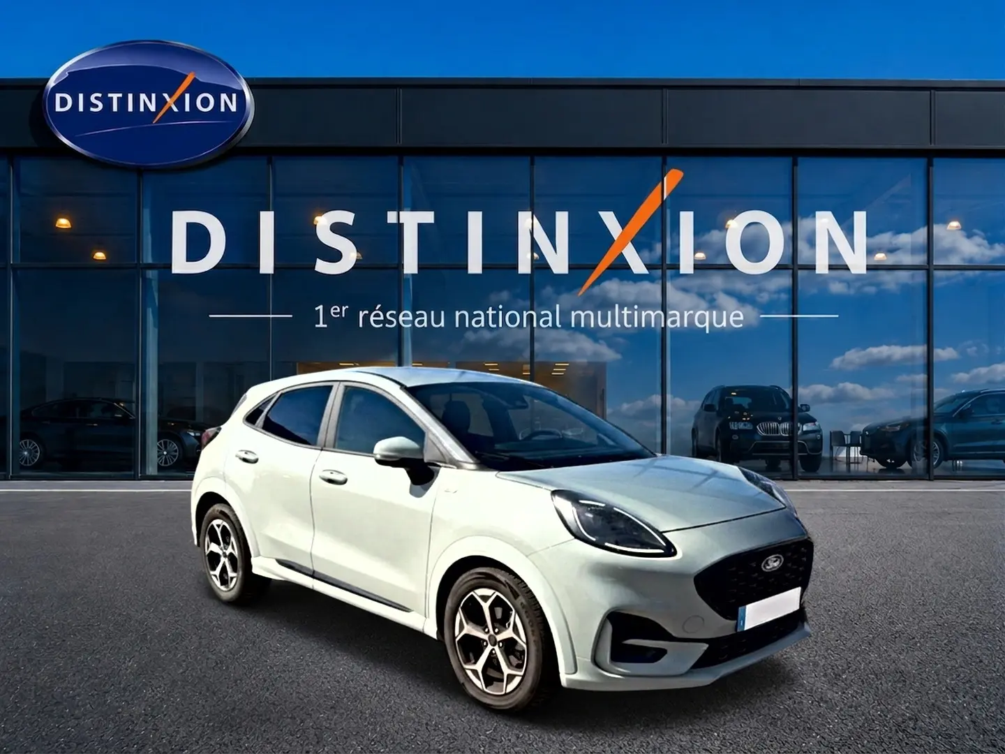 Ford Puma gris cactus en 3/4 avant droit, avec jantes alu et calandre noire, devant une vitrine Distinxion.