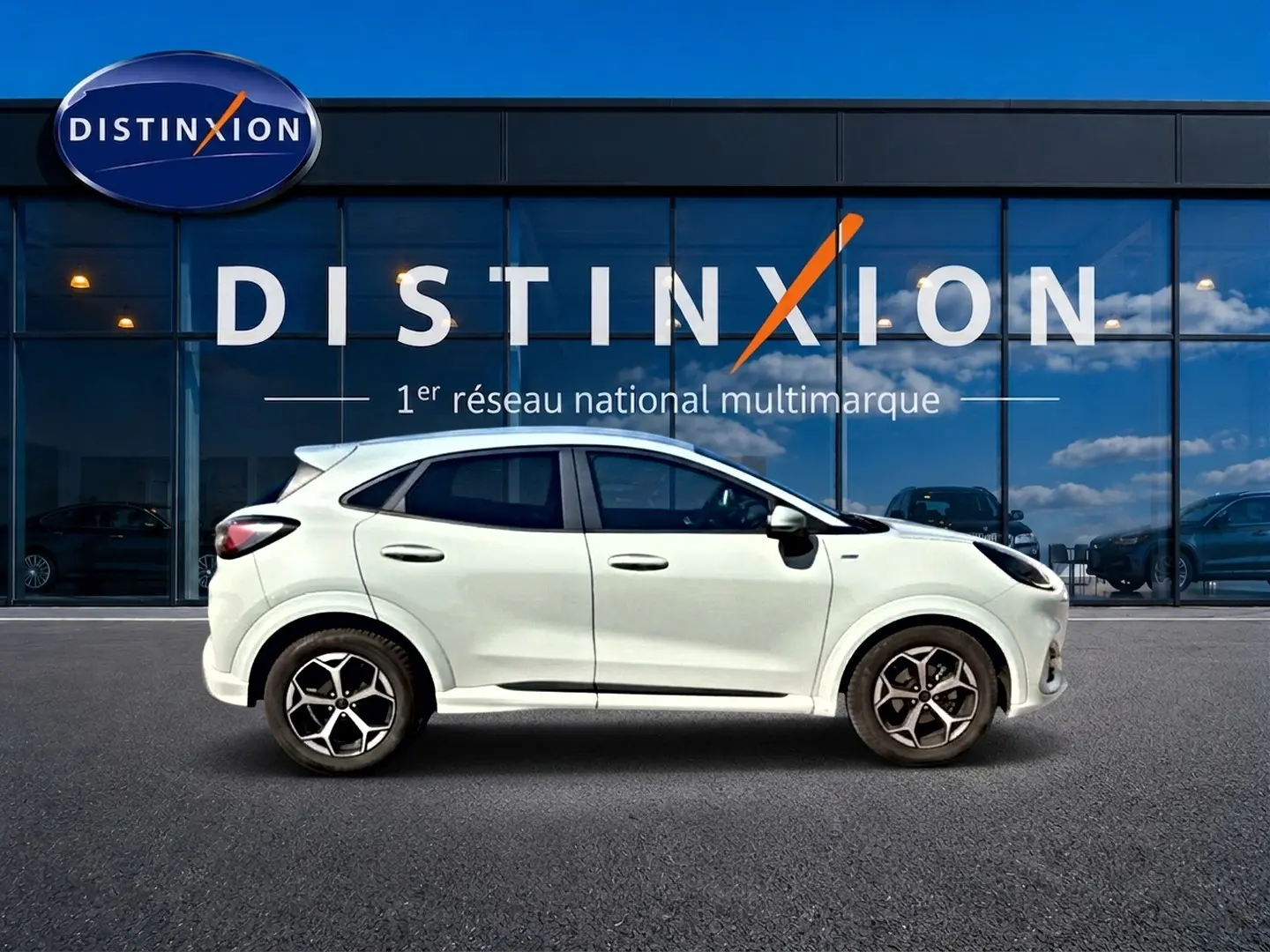 Vue de profil côté gauche du Ford Puma gris cactus garé devant une vitrine avec logo Distinxion.