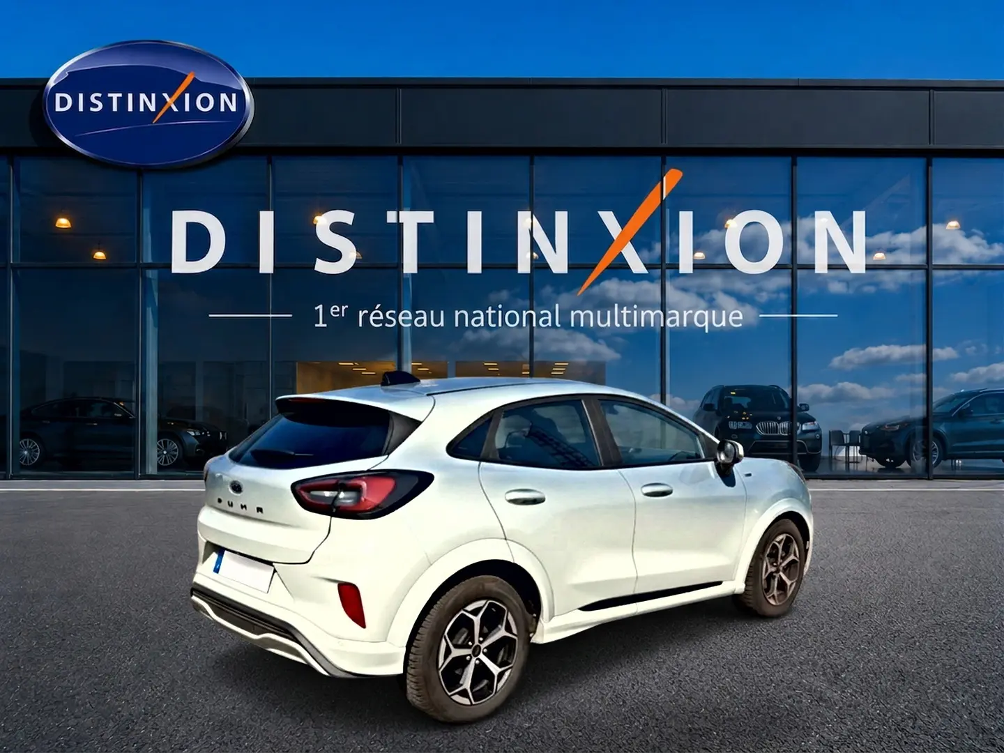 Vue 3/4 arrière droite d'une Ford Puma gris cactus 2025 devant une vitrine Distinxion, jantes alu visibles.