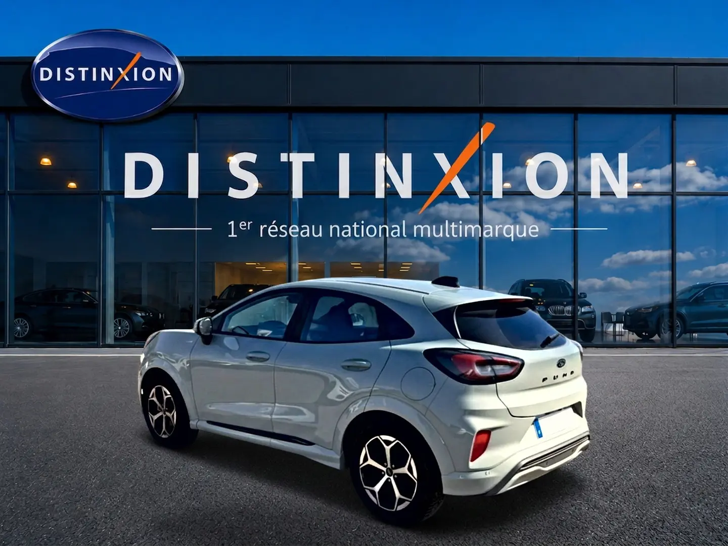 Ford Puma gris cactus vue 3/4 arrière droit, avec jantes alu et vitres arrière surteintées devant un showroom Distinxion.