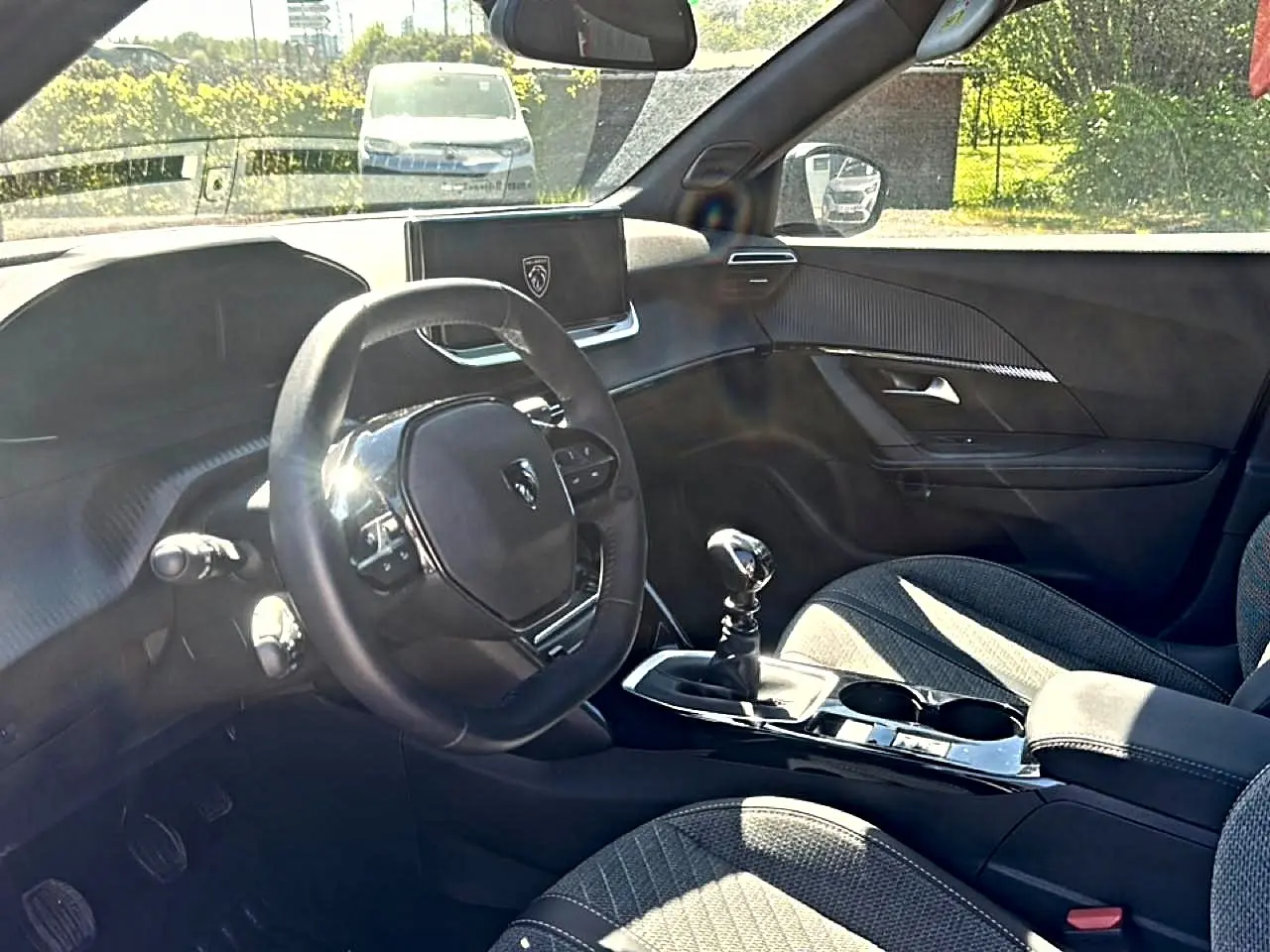 Vue intérieure côté conducteur du Peugeot 2008 2025, montrant le volant compact, la boîte manuelle et les sièges en tissu gris.