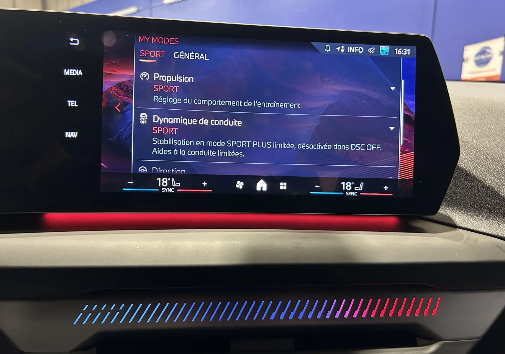Écran tactile central de la BMW Série 1 120DA 2024 affichant les modes de conduite sport avec éclairage d'ambiance rouge et bleu.