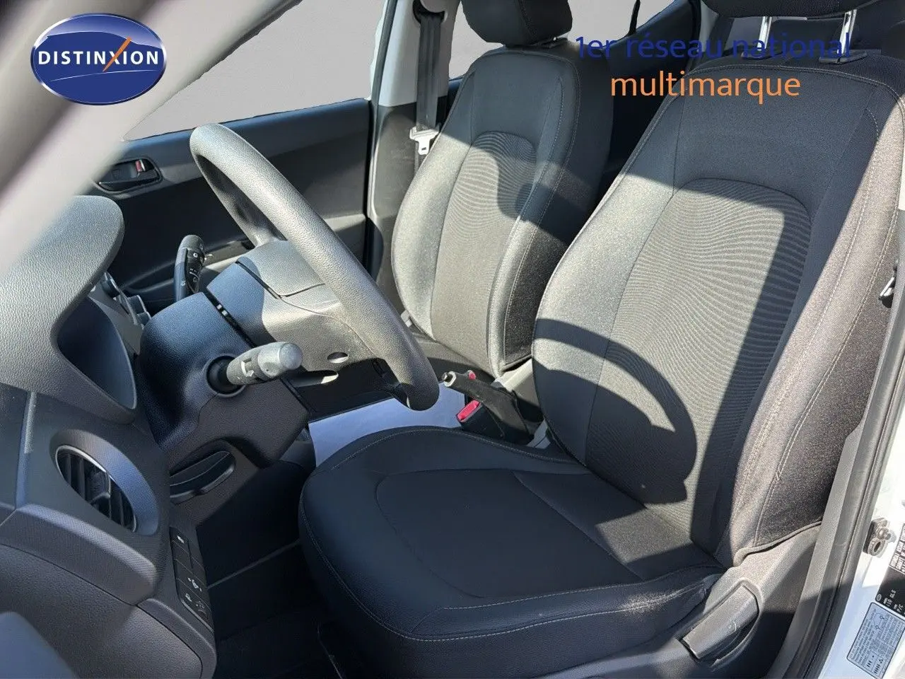 Intérieur de la Hyundai i10 blanche 2018, vue côté conducteur montrant les sièges noirs et le volant.
