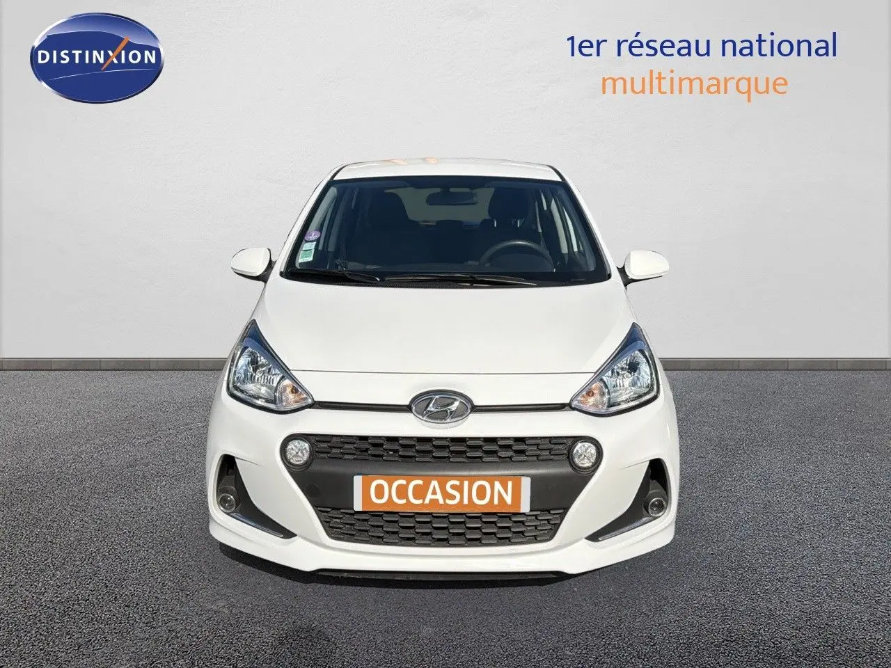 Vue de face d'une Hyundai i10 blanche 2018 avec calandre noire et plaque "OCCASION" orange visible.