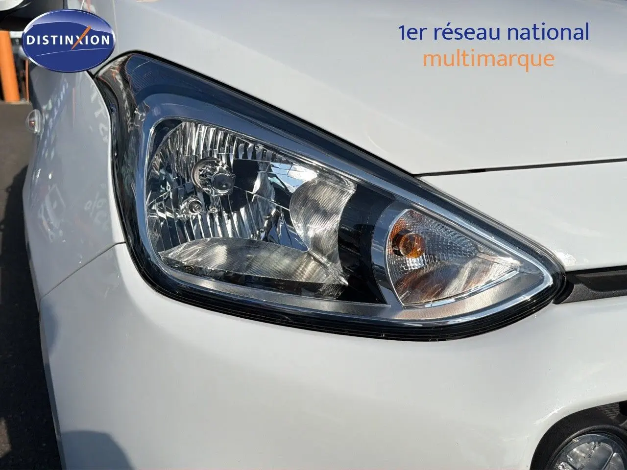 Gros plan sur le phare avant droit d'une Hyundai i10 blanche de 2018, soulignant les détails du bloc optique.