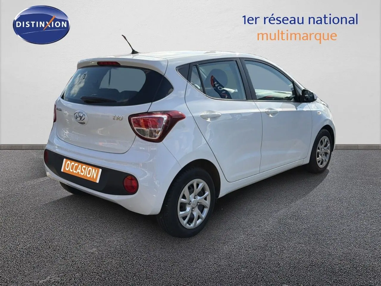 Vue 3/4 arrière droite d'une Hyundai i10 blanche 5 portes, avec feux arrière distinctifs et antenne de toit.