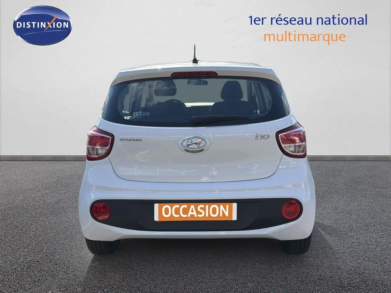 Vue arrière d'une Hyundai i10 blanche 2018 avec feux rouges et plaque d'occasion visible sur un sol gris.