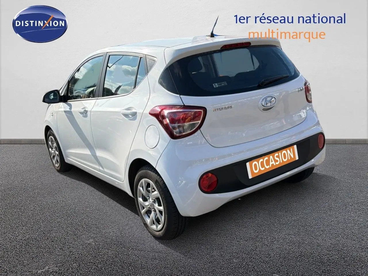 Vue 3/4 arrière droite d'une Hyundai i10 blanche 2018, compacte avec hayon et feux arrière distinctifs.