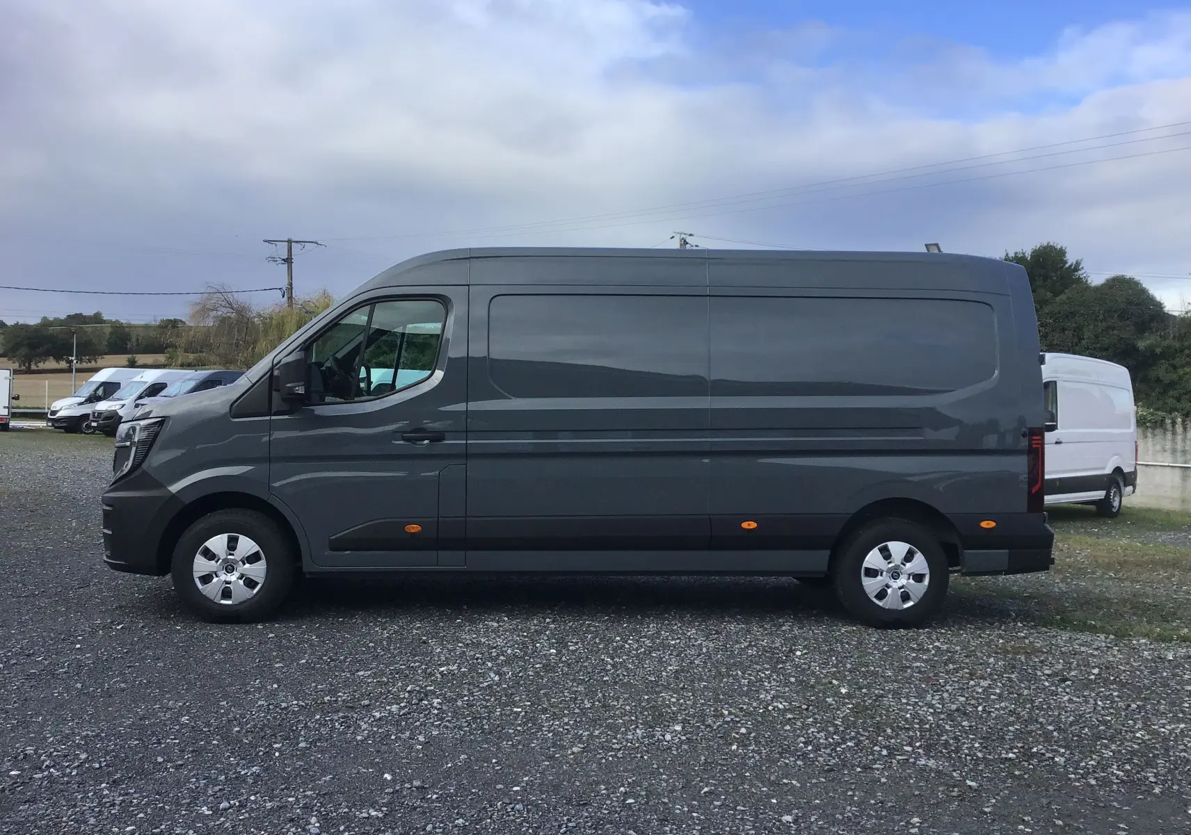 Vue de profil côté gauche du Renault Master L3H2 gris urbain 2025, avec marquages latéraux et feux arrière visibles.