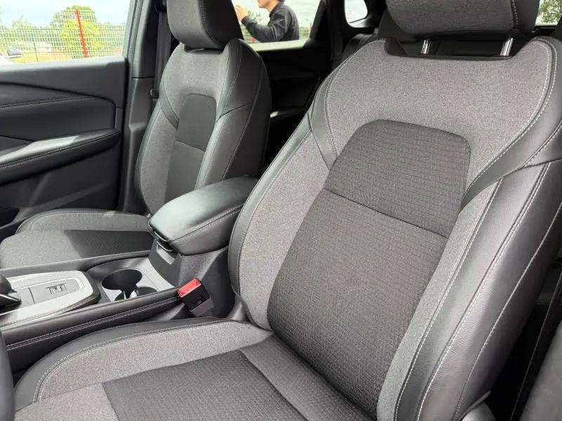 Vue rapprochée des sièges avant en tissu mixte noir et gris du Nissan Qashqai 2025, avec accoudoir central et console.