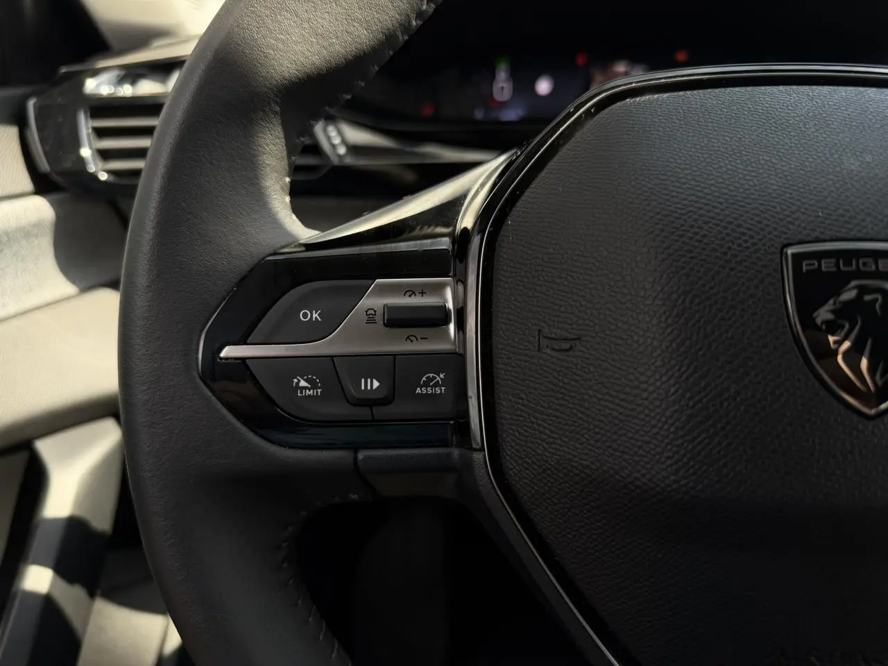 Gros plan sur le volant cuir noir de la Peugeot 308 2025, avec commandes du régulateur et logo lion central.