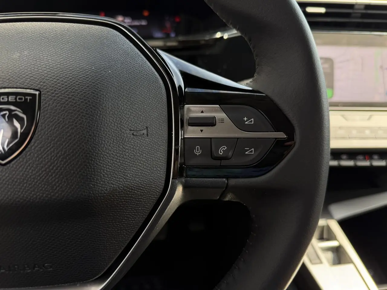 Gros plan sur le volant cuir noir de la Peugeot 308 2025 avec commandes intégrées et tableau de bord numérique en arrière-plan.