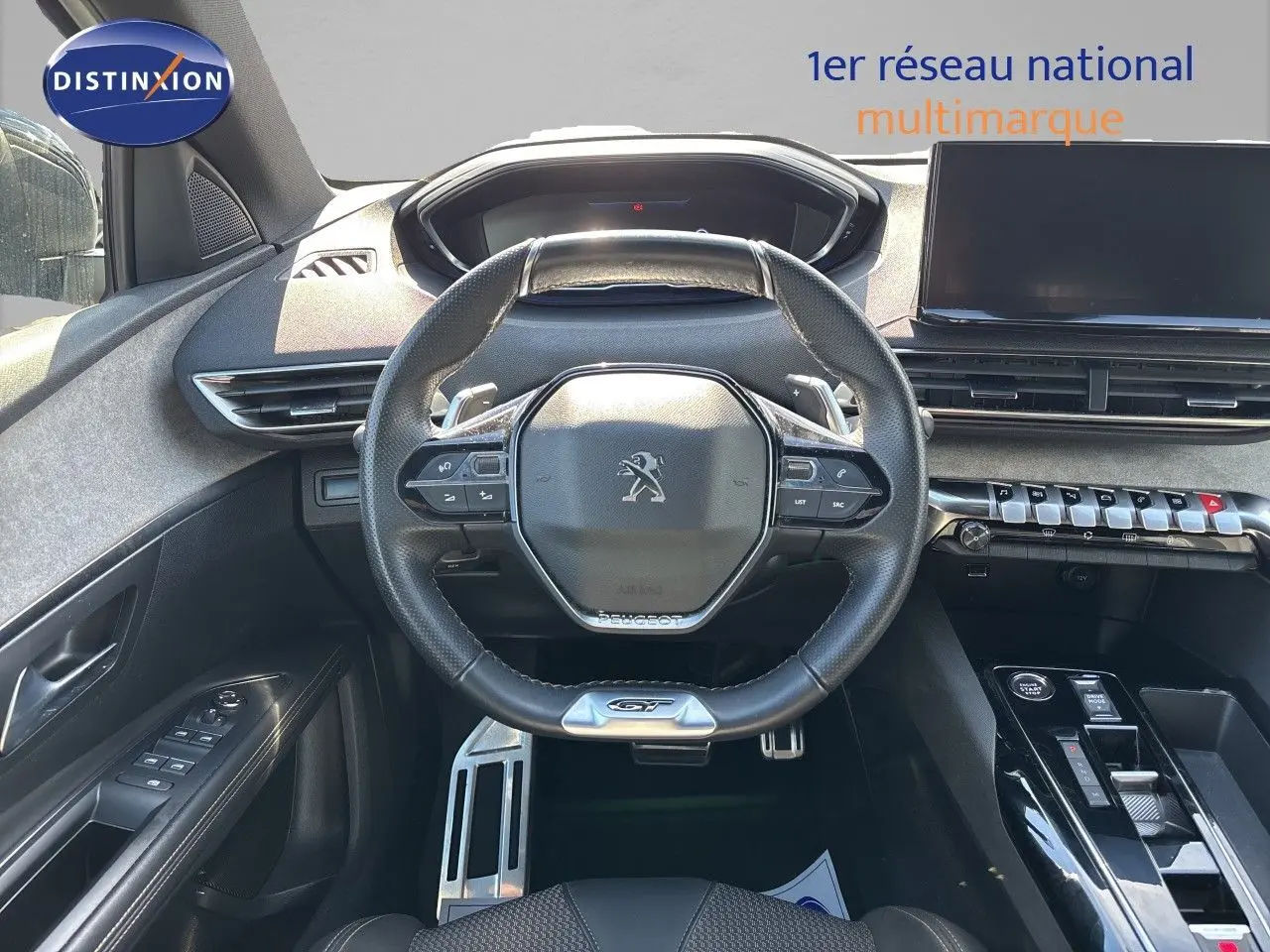 Vue intérieure frontale du poste de conduite du Peugeot 5008 GT 2023, volant compact cuir noir avec logo lion.